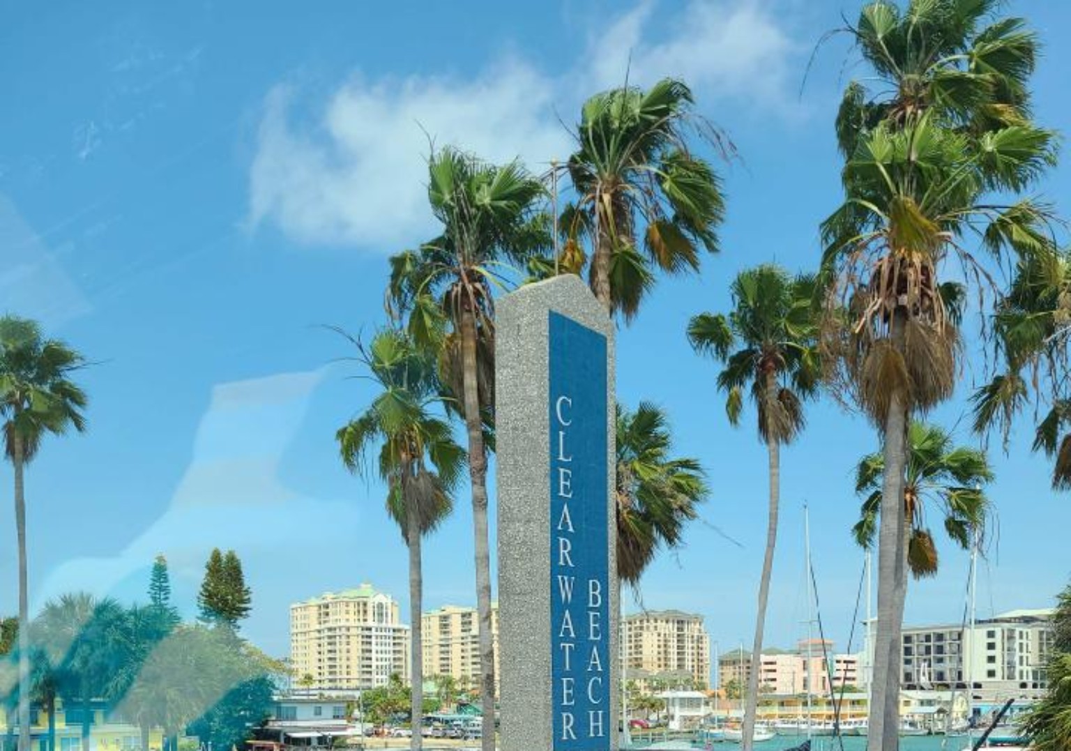 Clearwater Beach entrance sign framed by palm trees and waterfront buildings.